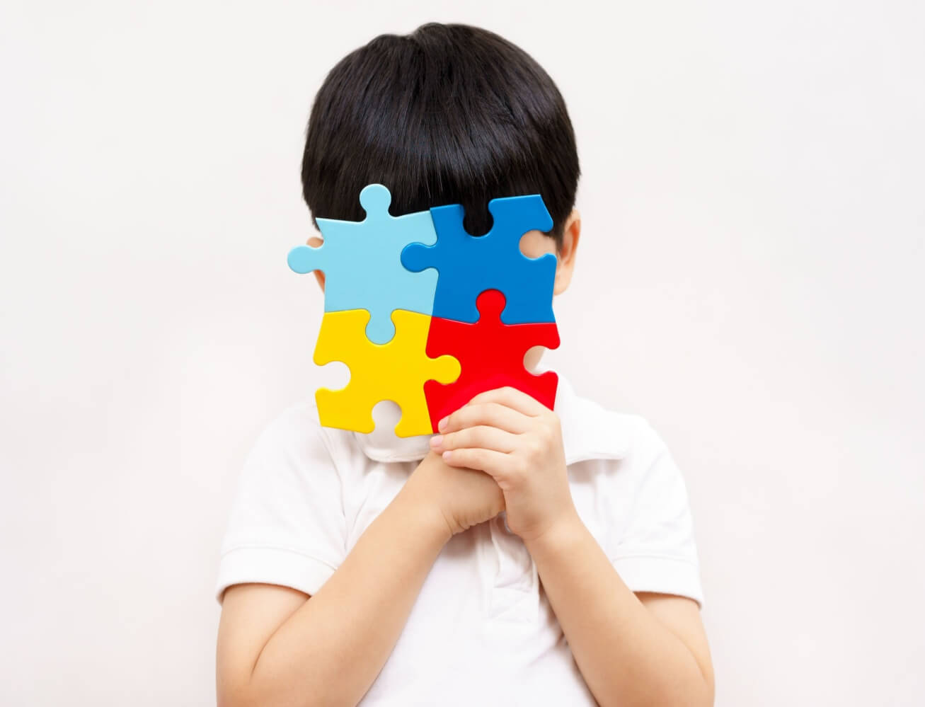 Studio Portrait of a little cute asian child cover his face with the colorful puzzles pieces