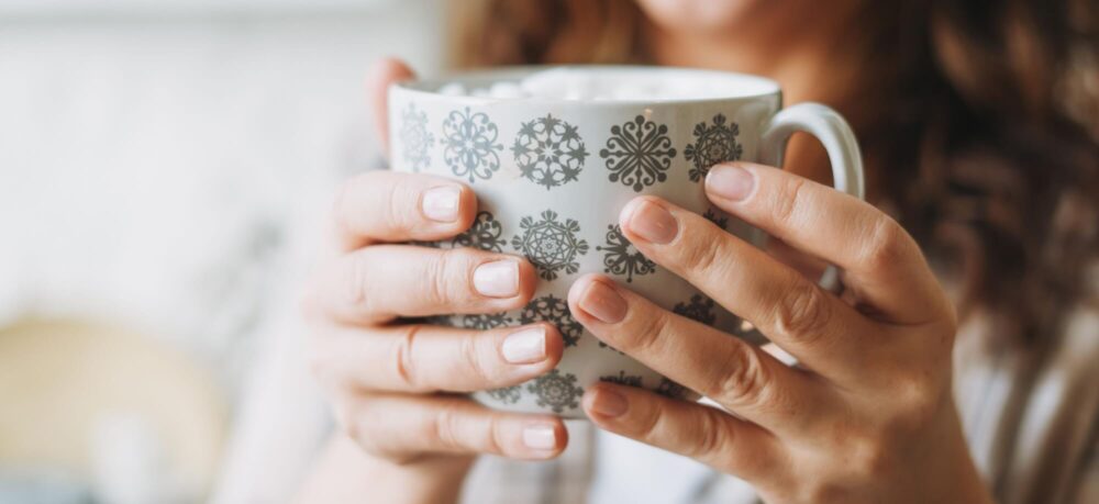 Attractive smiling woman with curly hair in plaid shirt with cup of cacao with marshmallow, cozy winter christmas mood