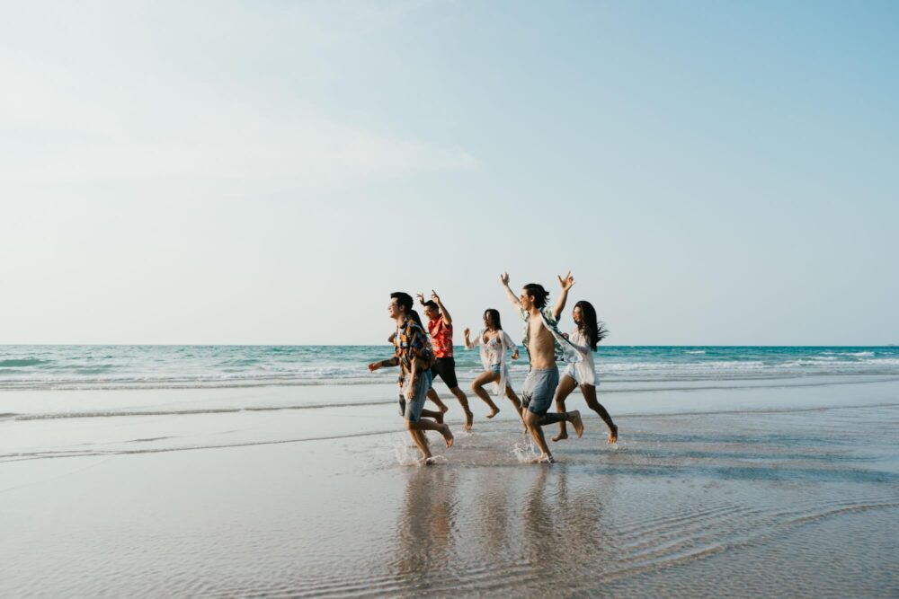 Group of friends running having fun on the white sand beach amid the blue sky