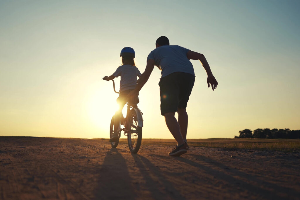 A father and daughter are riding their bikes in the sun