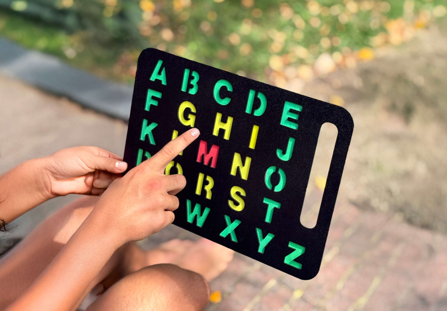 a person pointing to a letter on a black alphabet letterboard
