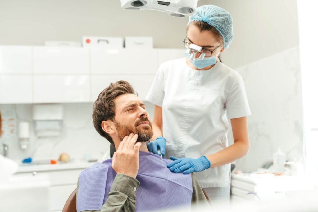 Portrait of attractive male patient sitting in dental chair, touching his cheek