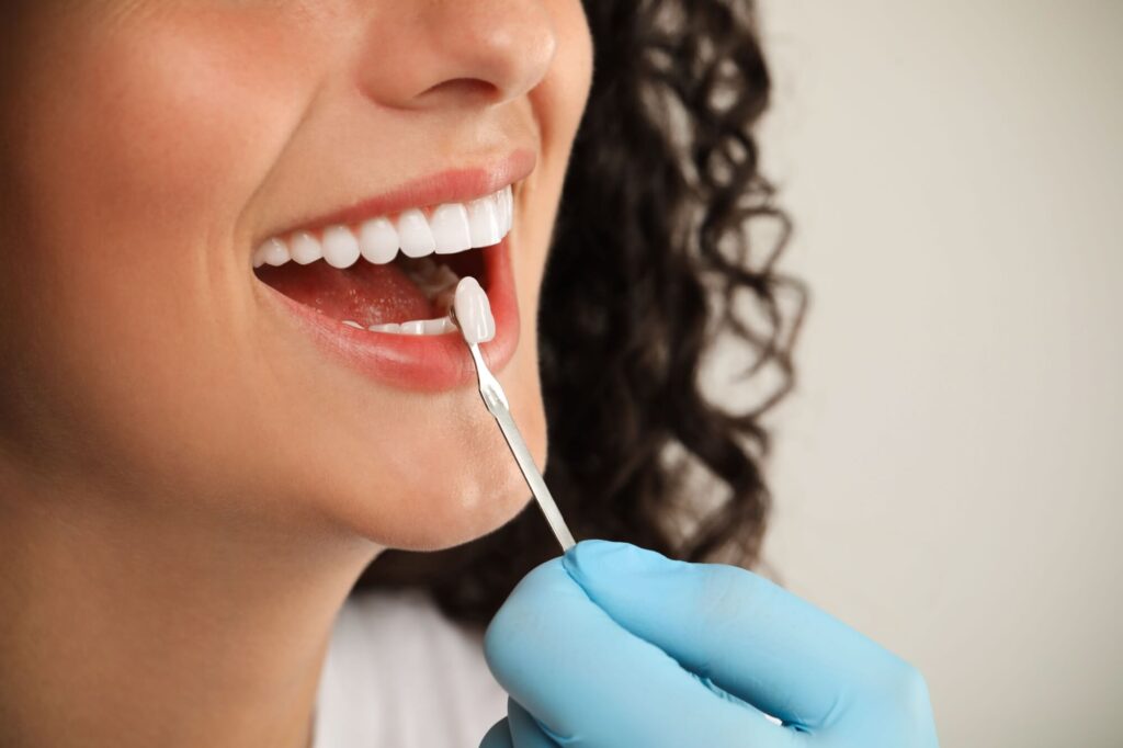 Doctor checking young woman's teeth color on light grey background,