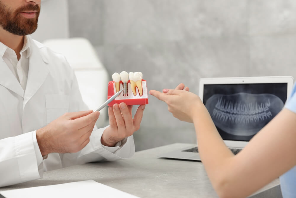 Doctor showing patient educational model of dental implant in clinic