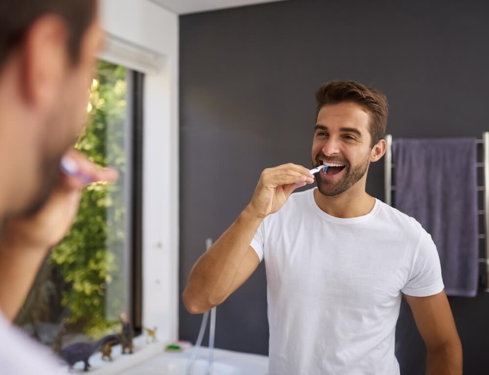 Man, smile and brushing teeth in mirror of bathroom for oral hygiene