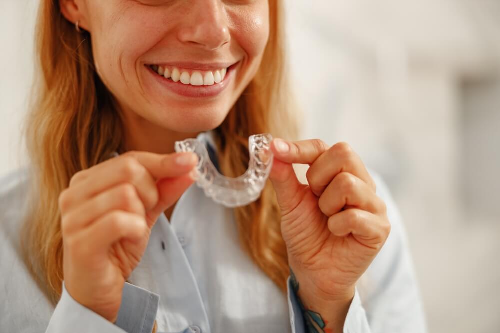 A joyful woman holds up her clear dental aligner