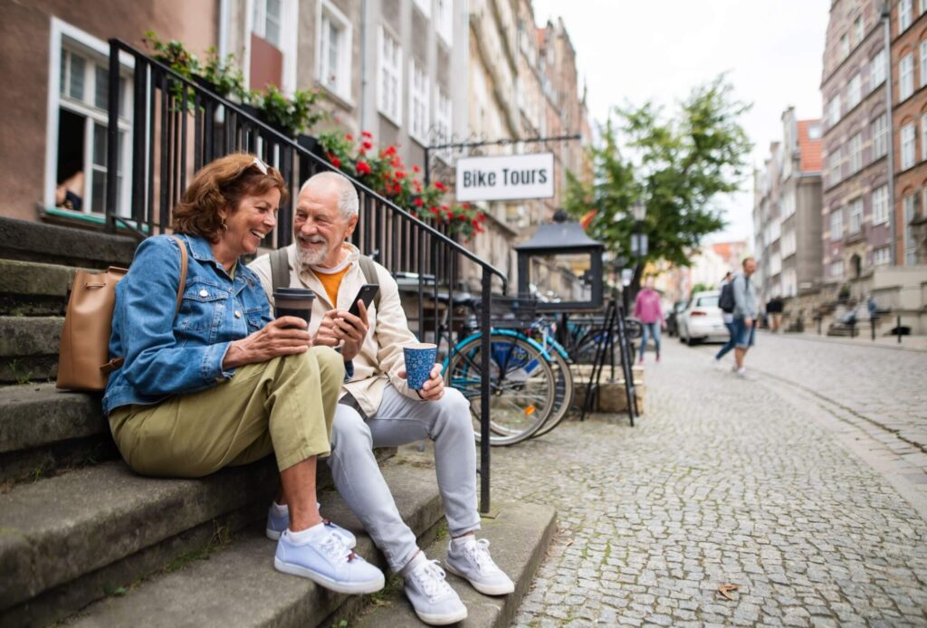 Happy senior couple tourists sitting on stairs and having take away coffee