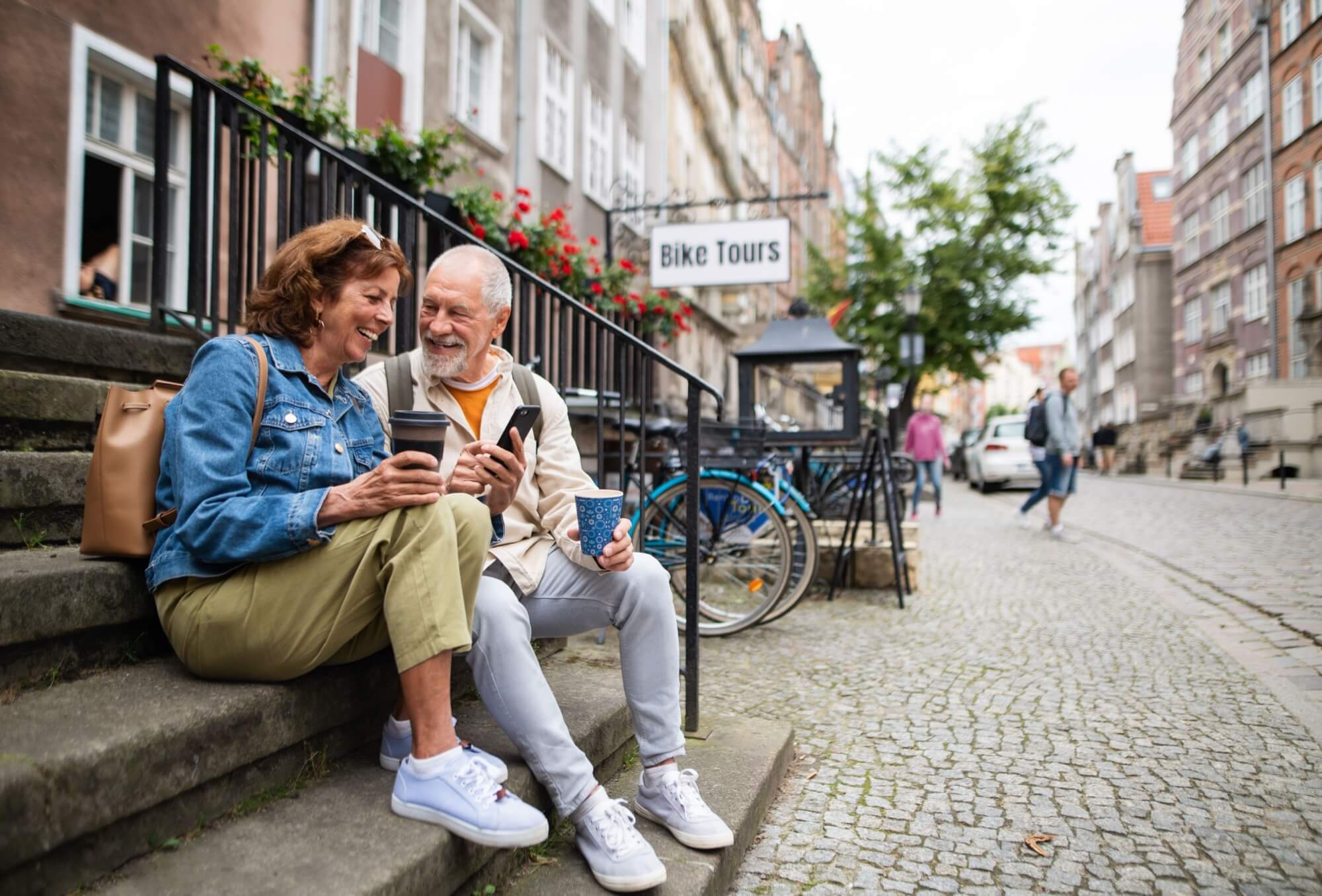 Happy senior couple tourists sitting on stairs and having take away coffee