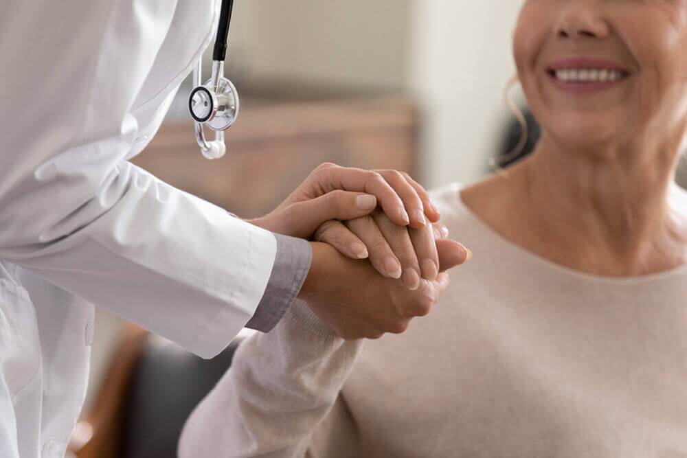 Close up shot of young female physician leaning forward to smiling elderly lady patient holding her hand