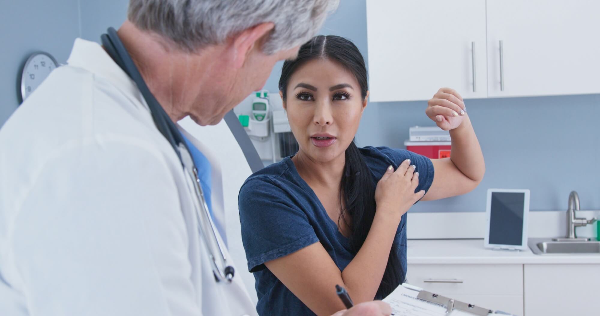 Japanese woman explaining shoulder pain to doctor in exam room