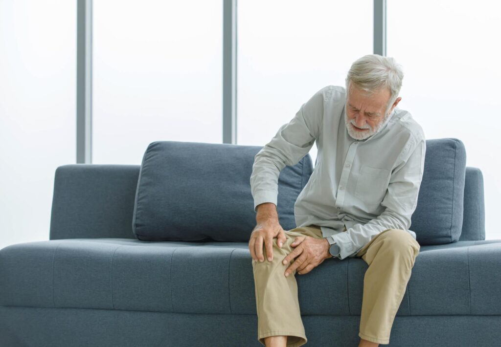 old senior sitting on sofa at home alone holding hands on knee