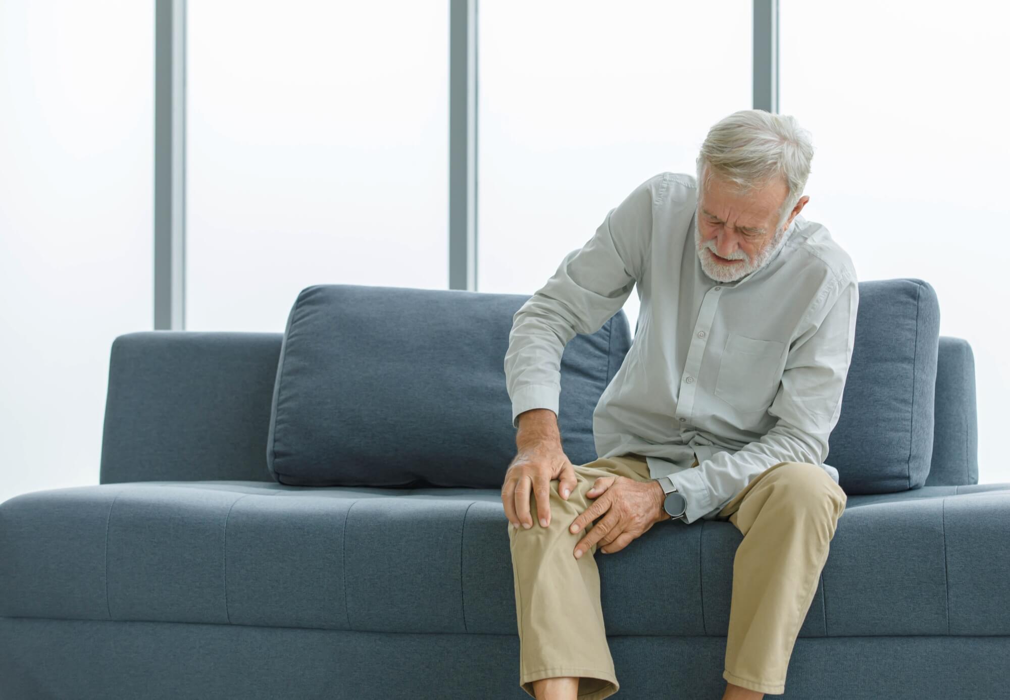 old senior sitting on sofa at home alone holding hands on knee