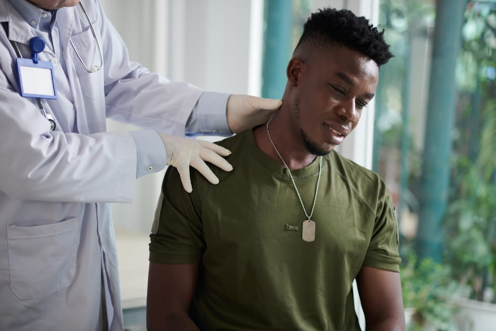 Young soldier feeling severe pain when doctor palpating his neck and shoulder
