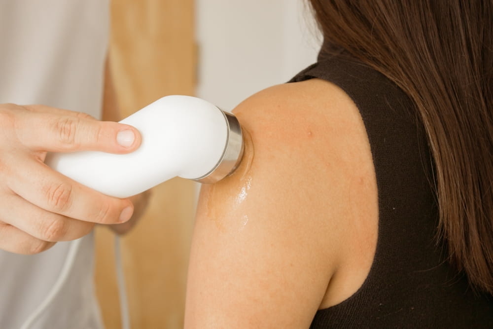 Hand of a physical therapist applying ultrasound on a patient's injured shoulder.