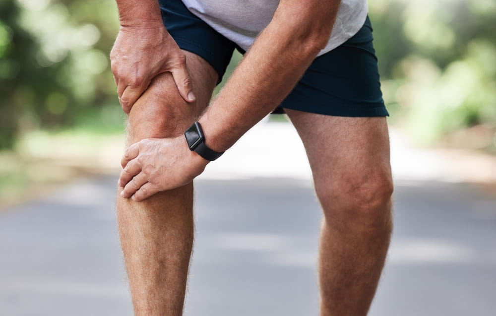 Running, knee pain and old man with hand on leg in park in for outdoor fitness and workout exercise.