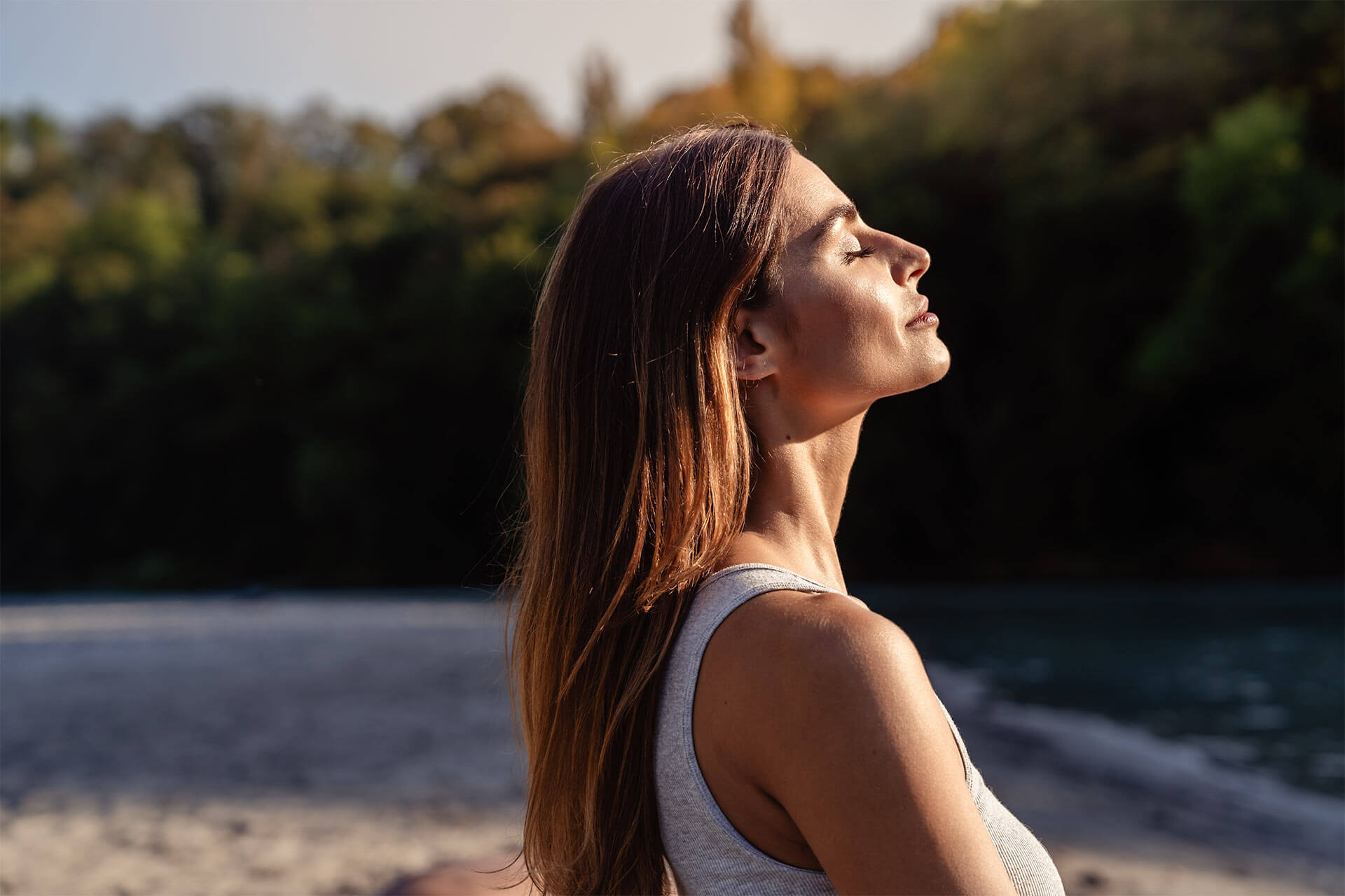 Young woman with long hair enjoying sun with closed eyes getting natural vitamin D outdoors