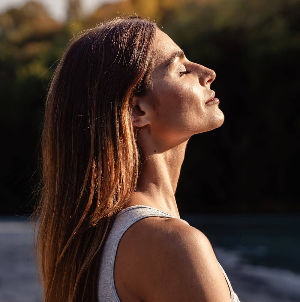 Young woman with long hair enjoying sun with closed eyes getting natural vitamin D outdoors