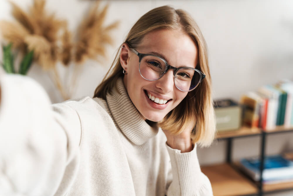 Photo of smiling attractive woman in eyeglasses taking selfie photo while sitting in cozy living room