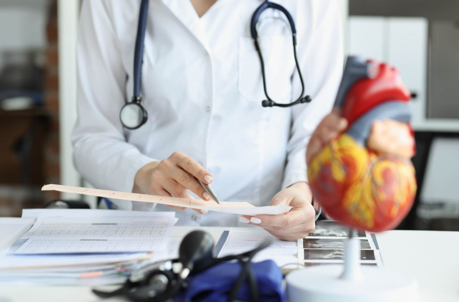 Doctor cardiologist examining cardiogram against background of artificial heart model