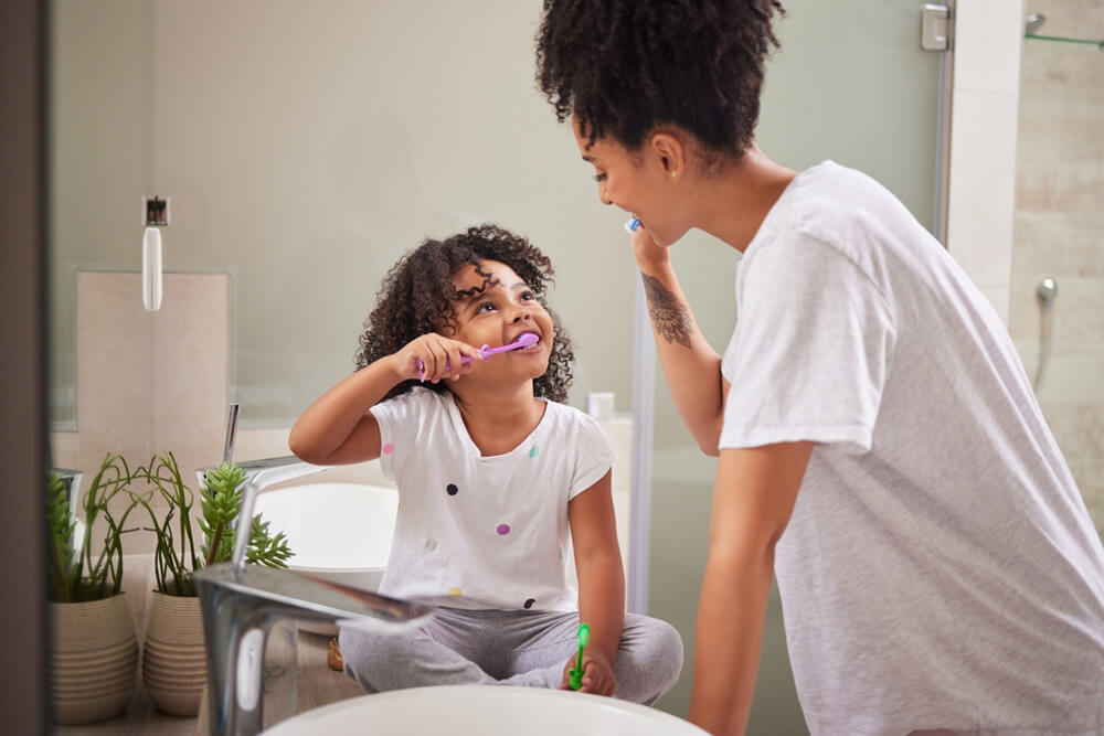 mother teaching child to brush teeth in bathroom