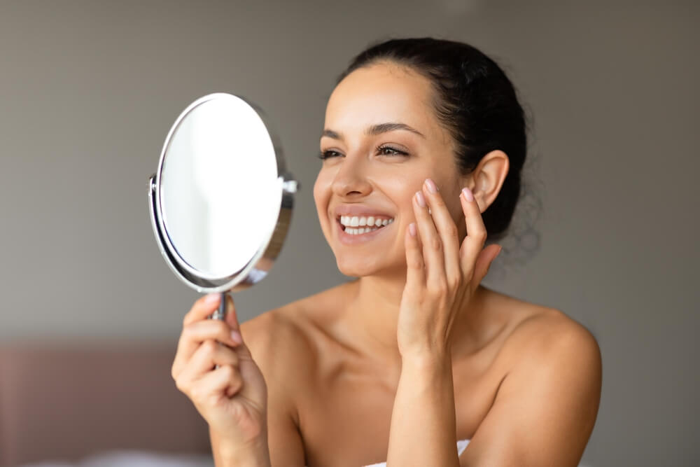 Cheerful young woman smiles while applying moisturizer