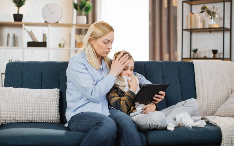 Pretty 40-aged woman mother sitting with her sick teen boy on soft sofa and watching together