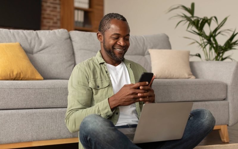 App for work, business remote. Happy middle aged african american male with laptop typing on phone
