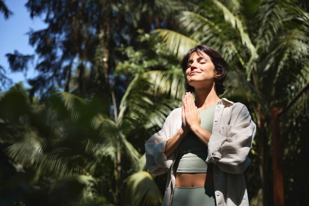 Hispanic woman holding hands in namaste meditating doing yoga breathing exercises
