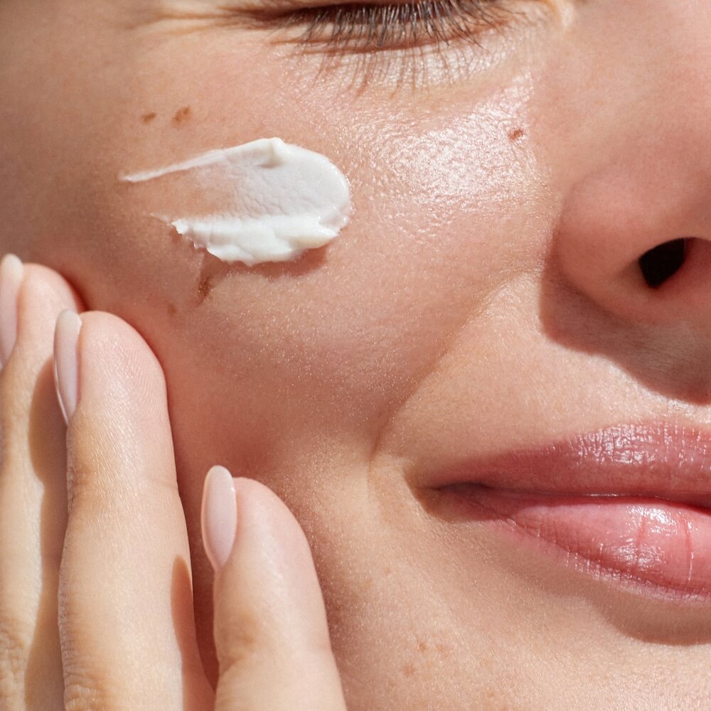 Hydration. Cream smear. Beuaty close up portrait of young woman with a healthy glowing skin is applying a skincare product.