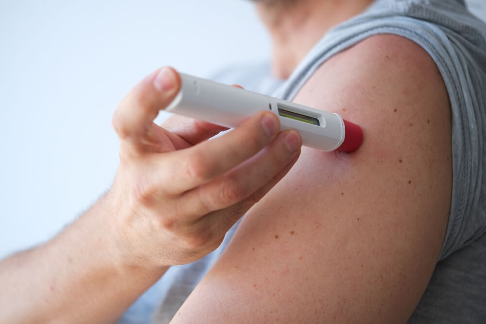 adult man injecting himself a treatment such as insulin or Adalimumab, Etanercept or epinephrine into his shoulder