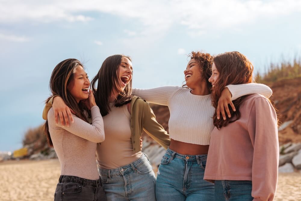 Female friends laughing and smiling at each other while wearing vintage clothes at the beach