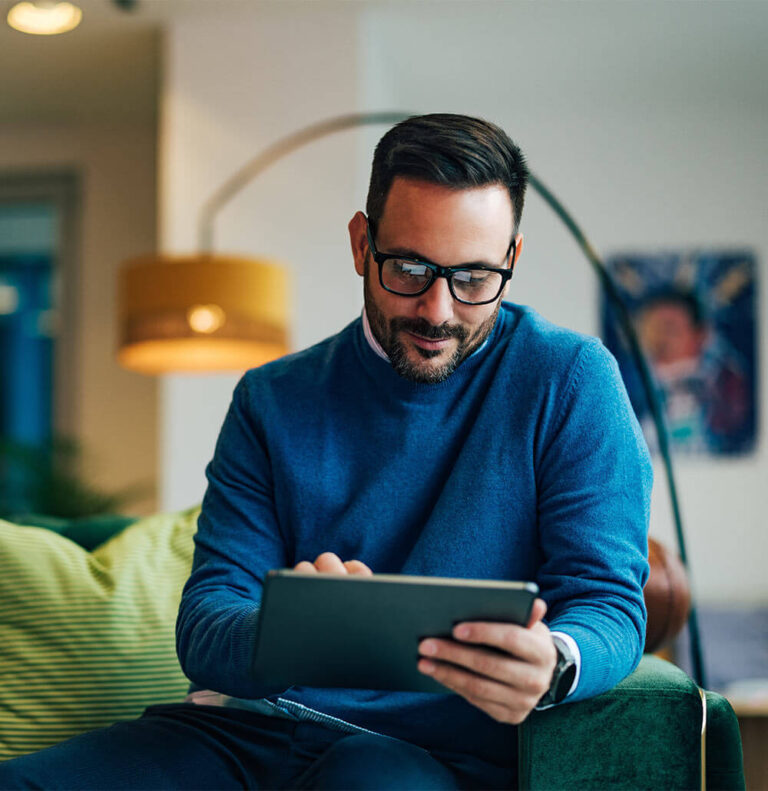 Positive man using a digital tablet while sitting on the couch