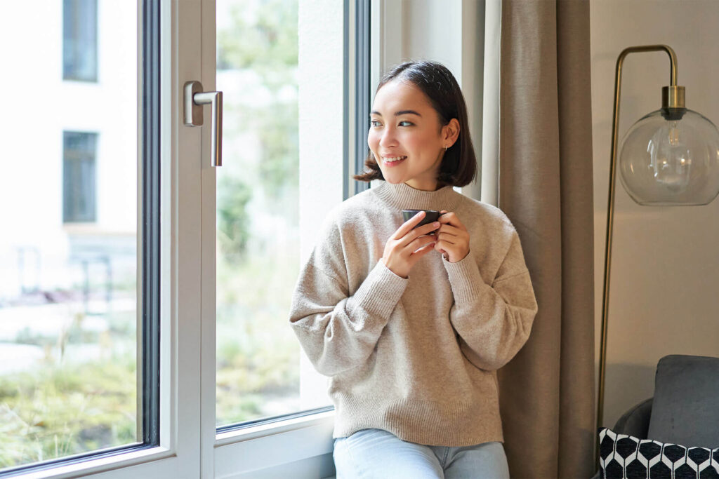 Beautiful young woman sitting near window and drinking her coffee