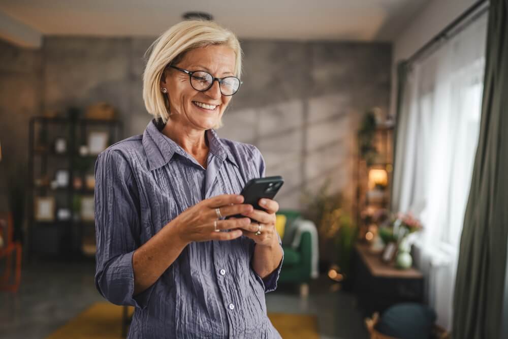 Mature woman stand and use mobile phone at home