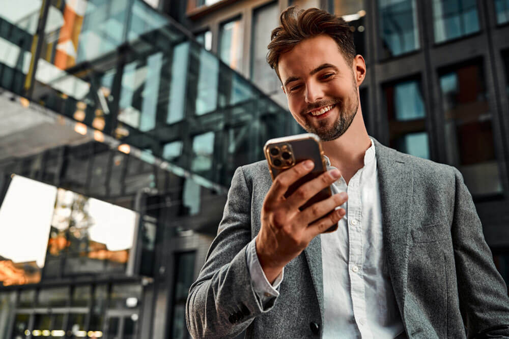 Confident smiling man holding a phone and standing outside