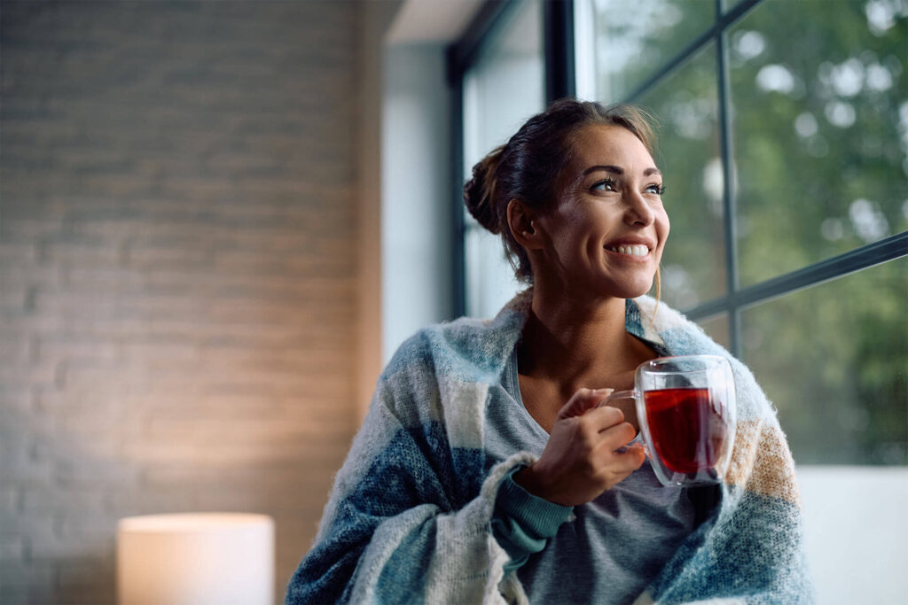 Happy woman enjoying cup of warm tea by the window