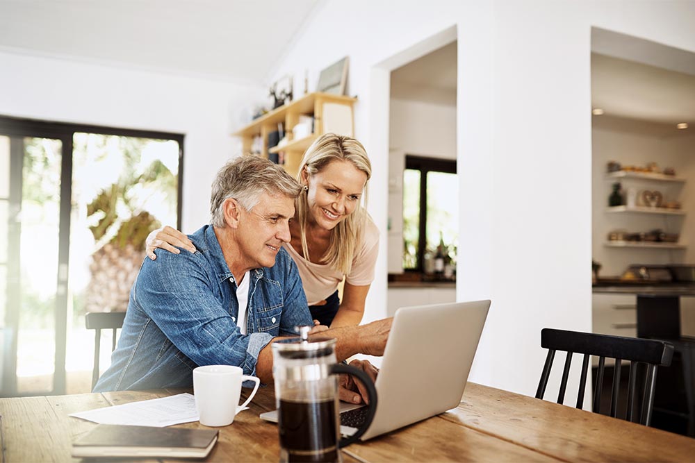 Couple with laptop planning finance, banking and checking retirement budget while becoming debt free at home