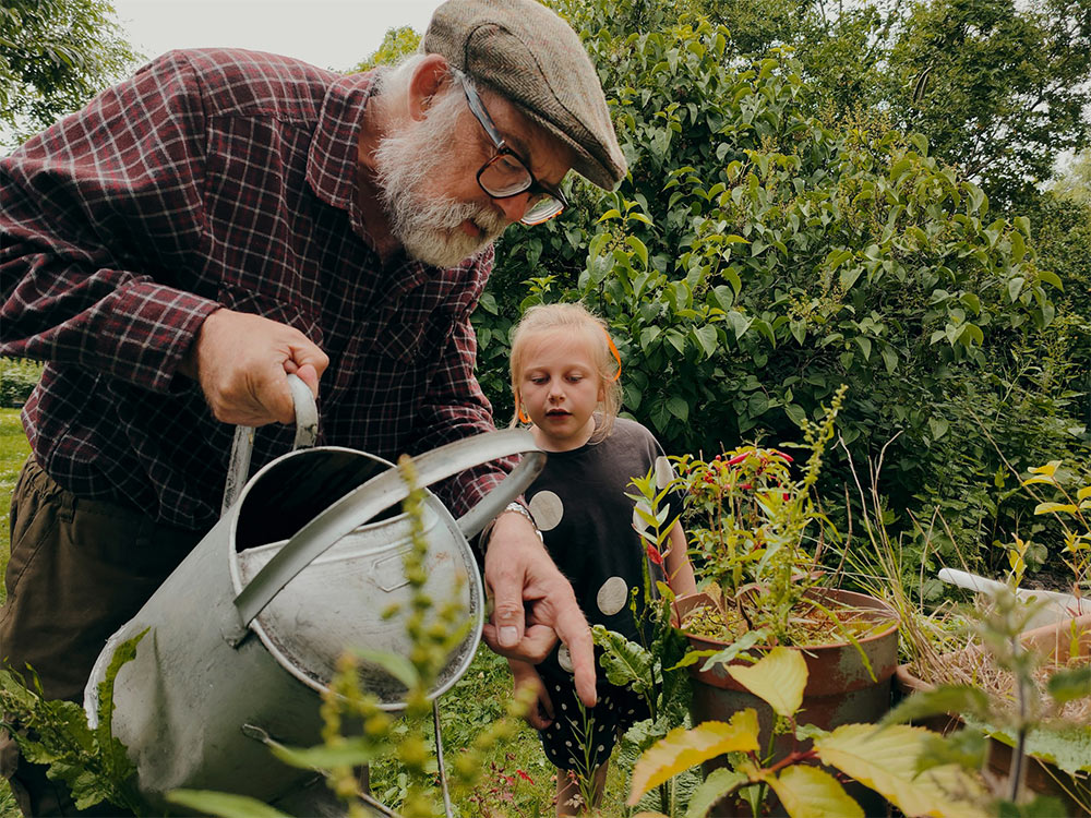 elderly man watering plants with his grand daughter