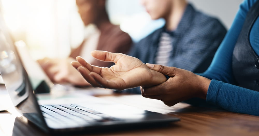 Business person, hands and laptop with wrist injury or pain for carpal tunnel syndrome in office.