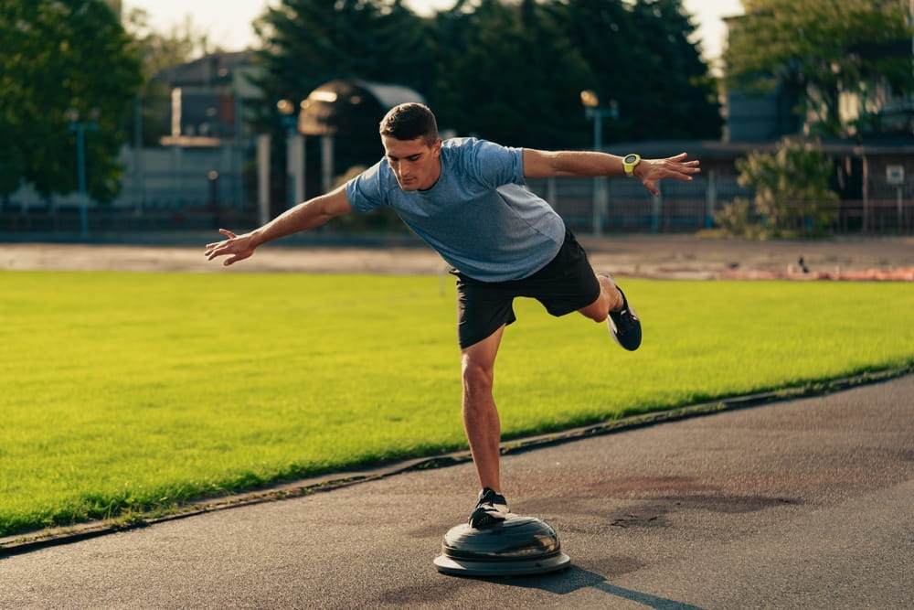 Man practicing balance on a stability board at an outdoor sports facility during daylight hours