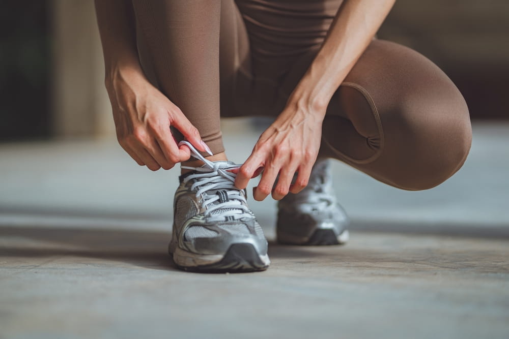 Close-up of female runner tying shoelaces on running sneakers before summer workout in the city – fitness and wellness lifestyle concept