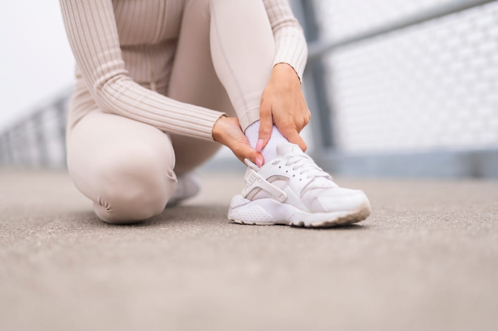 Woman feeling sharp ankle pain, grabbing her achilles tendon outdoors