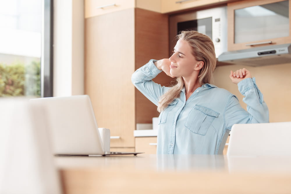 Smiling pretty young woman meets morning in kitchen, checks mail using laptop and high speed internet