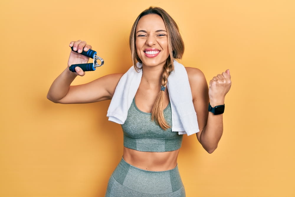 Beautiful hispanic woman training muscle with hand grip screaming proud, celebrating victory and success very excited with raised arm