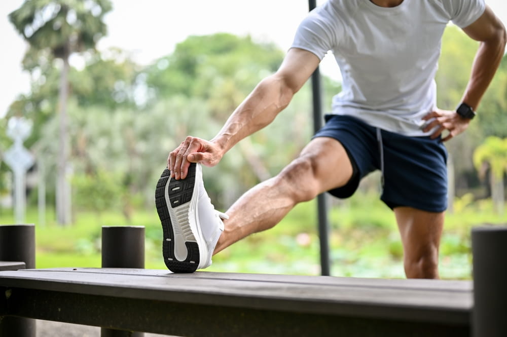 Athletic fit Asian man in sportswear is stretching his leg on a bench, warming up before running or cooling down after a long run. cropped image