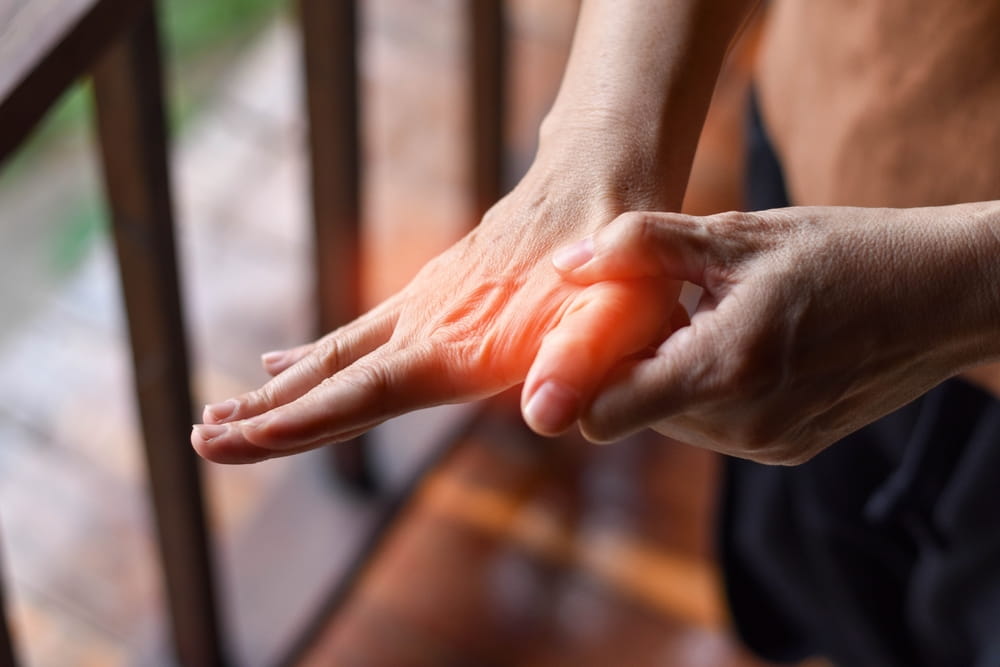 Hand pain shown by a person holding their wrist, with a red highlighted area indicating inflammation or discomfort, possibly from arthritis, strain, or joint-related issues.