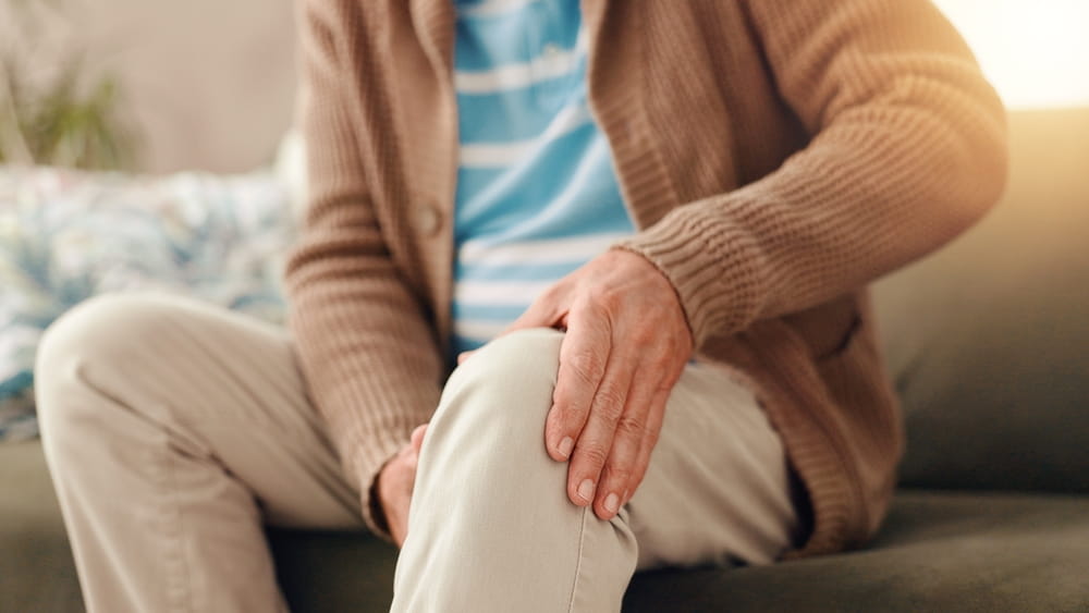 Senior man, sofa and knee pain with injury for chronic illness, arthritis or fibromyalgia at home.