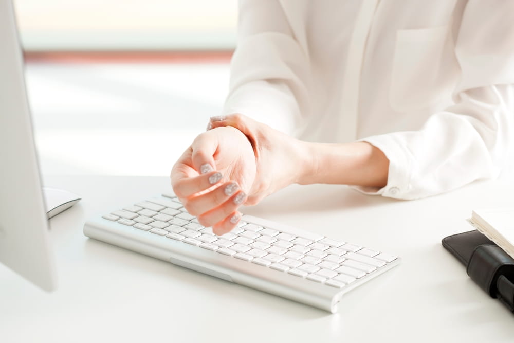 Wrist pain after long hours of typing at a computer desk in a bright and modern office setting during the day