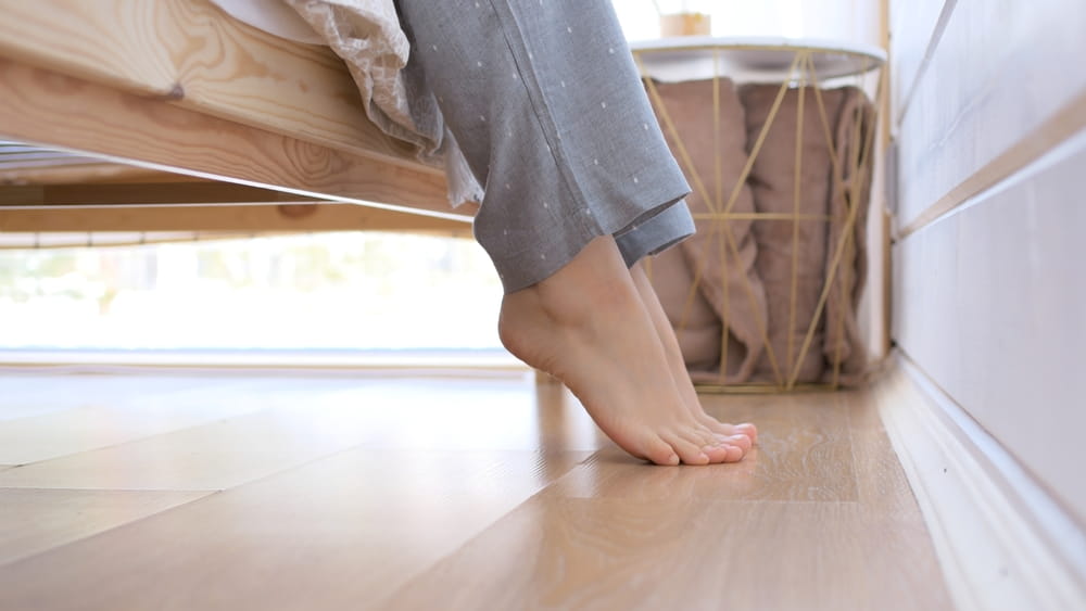 Close-up of female bare feet go along the floor in the bedroom to the bed and goes to sleep on the bed.