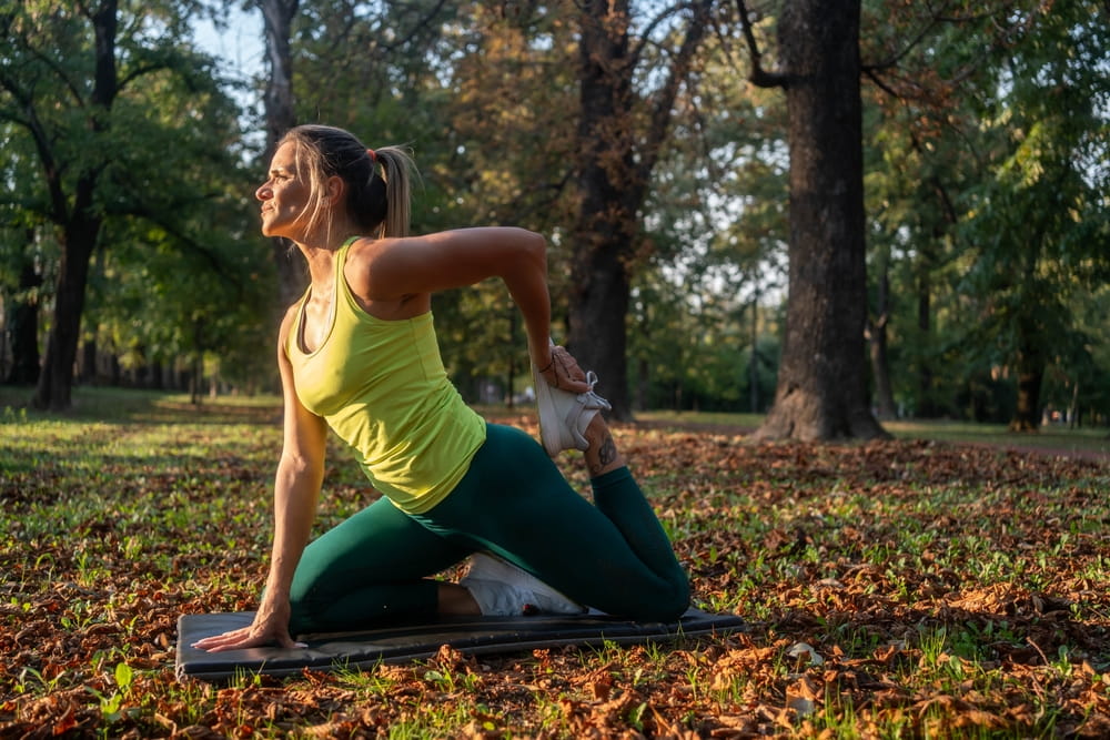 Fitness woman stretching legs doing pilates leg stretches exercises in outdoor park